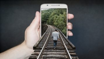 Person geht auf Gleis in Handybildschirm optische Täuschung