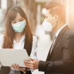Zwei Menschen mit Atemschutzmaske vor Stadthintergrund