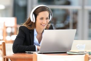 Frau mit Kopfhörern sitzt am Laptop und lacht