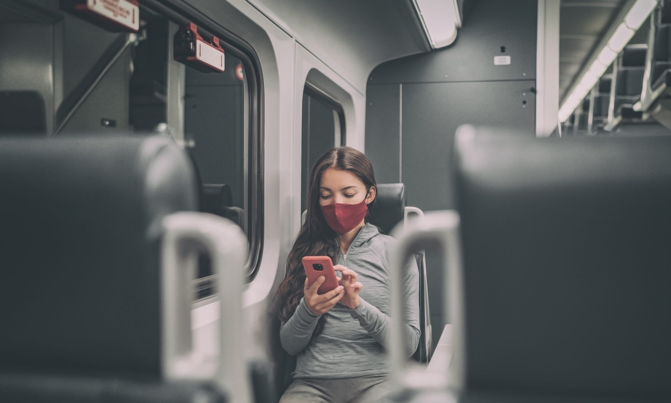 Junge Frau mit Maske sitzt alleine im Zug