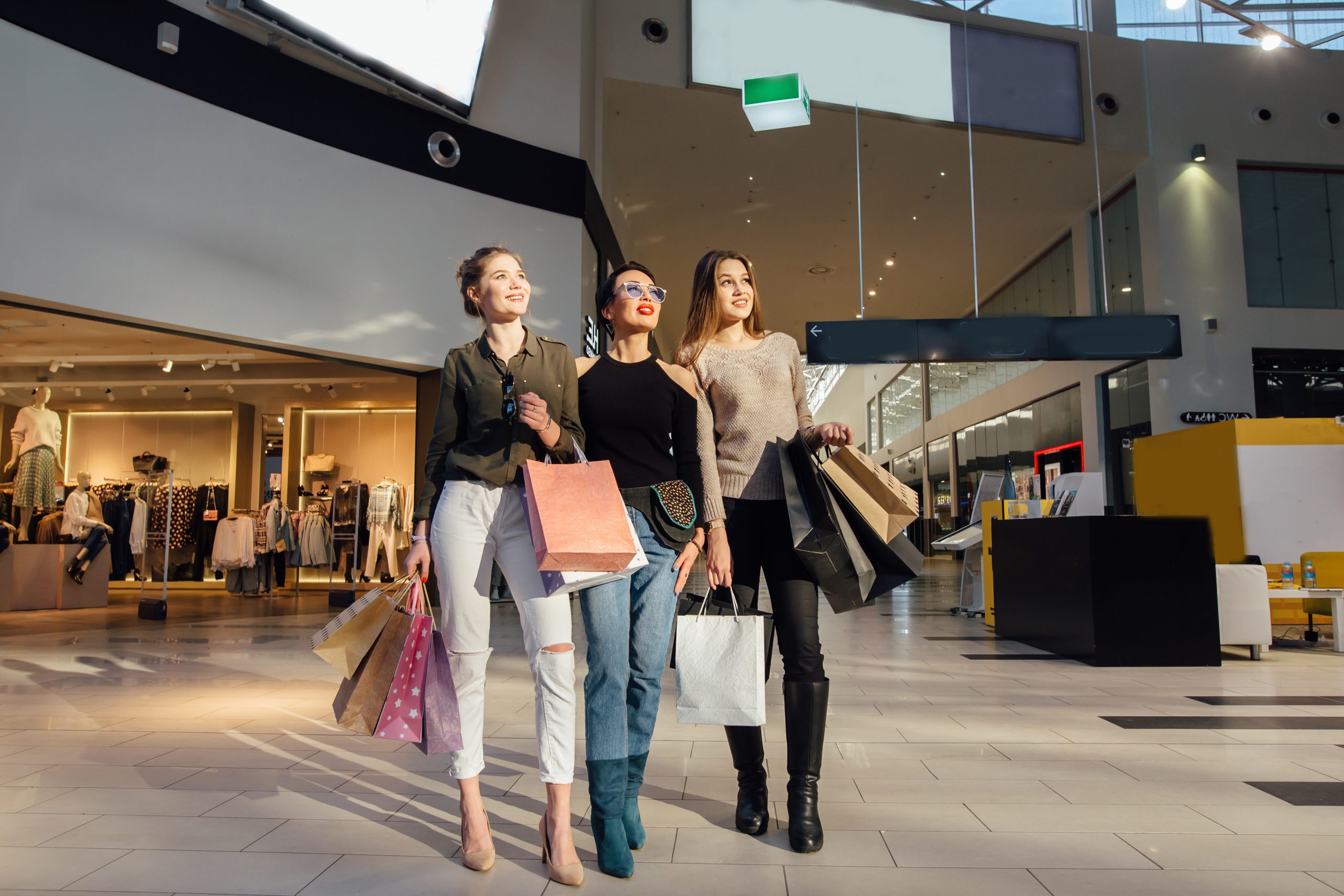drei bezaubernden Freundinnen mit Einkaufstaschen in einem Einkaufszentrum