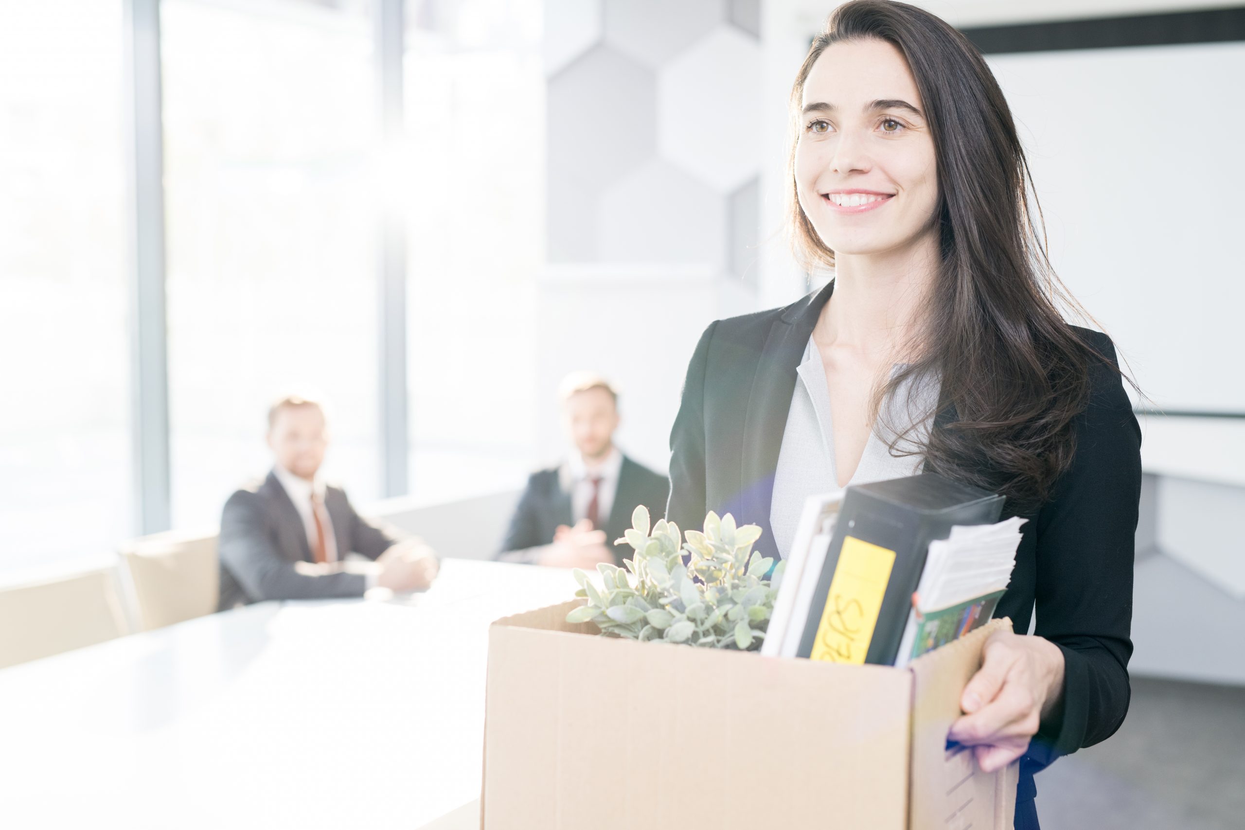 Jungen Geschäftsfrau, die eine Kiste mit persönlichen Gegenständen in der Hand hält, als sie ihr Büro verlässt