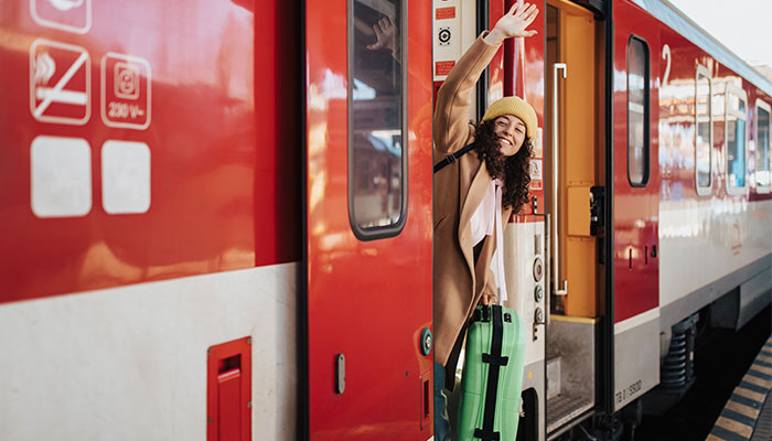 Junge Frau glücklich mit Koffer winkt aus Tür im Regionalzug