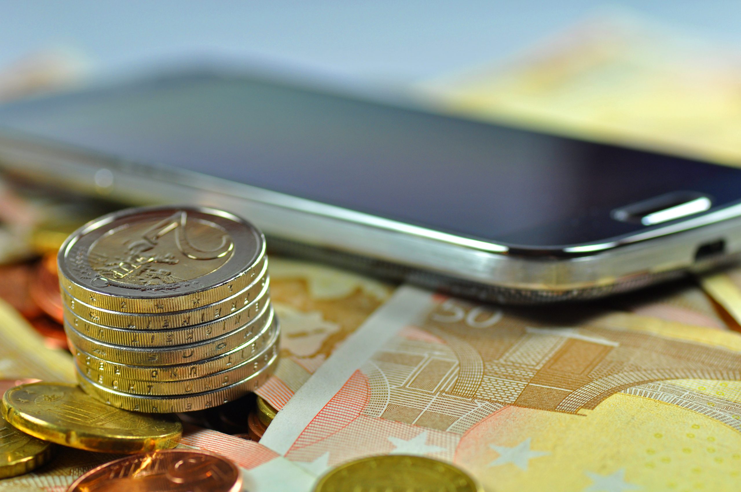 Smartphone liegt auf Geldscheinen und Münzenturm daneben