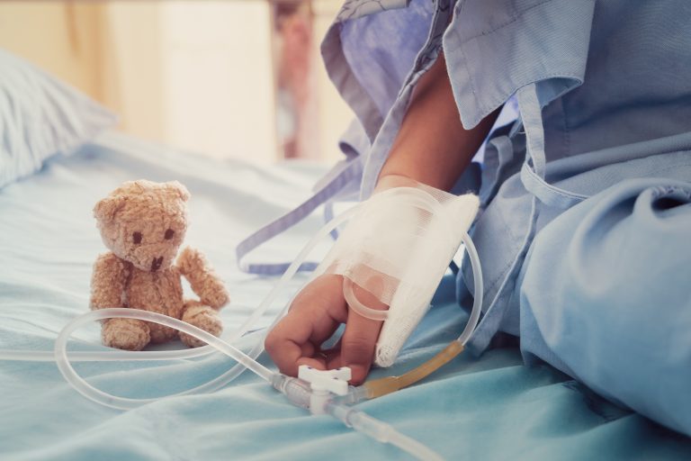 Soziales Engagement -  Verbundene Kinderhand und Teddy auf Krankenhausbett