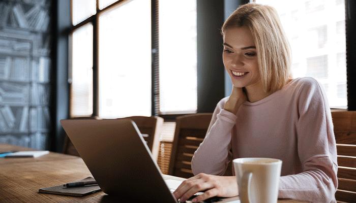 junge Frau sitzt lächelnd vor ihrem nimmt mit Laptop. Offenbar ist sie zufrieden mit ihrer alternativen Incentivierung