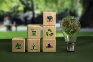 3 Stapel mit Holzblöcken mit verschiedenen Umwelticons und Glühbirne mit Zweig darin symbolisieren Notwendigkeit für Nachhaltigkeitsziele innerhalb der Unternehmensziele