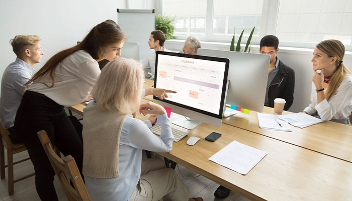 Online-Befragungen in Unternehmen. Mitarbeitende sitzen zusammen an einem Tisch und beantworten eine Online-Befragung.