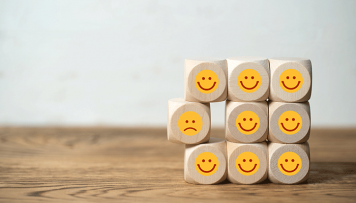 Mehrere Würfel sind übereinander gestapelt und haben Sticker mit teils lachenden und teils weinenden Smileys aufgeklebt. Diese symbolisieren die Kundenbefragung.