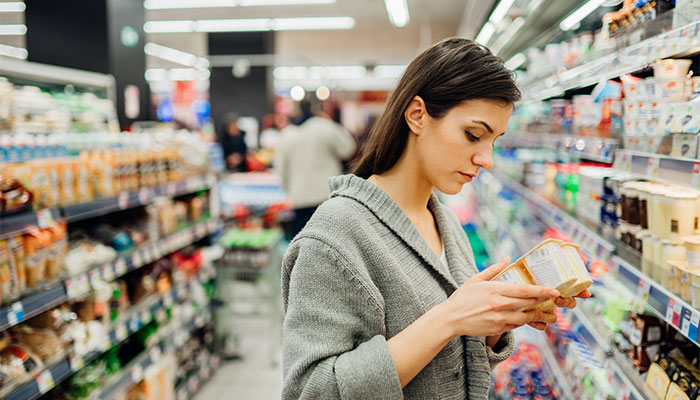 Angewandte Preisforschung: Eine Frau steht in einem Supermarkt und vergleicht Joghurts nach Preisen.