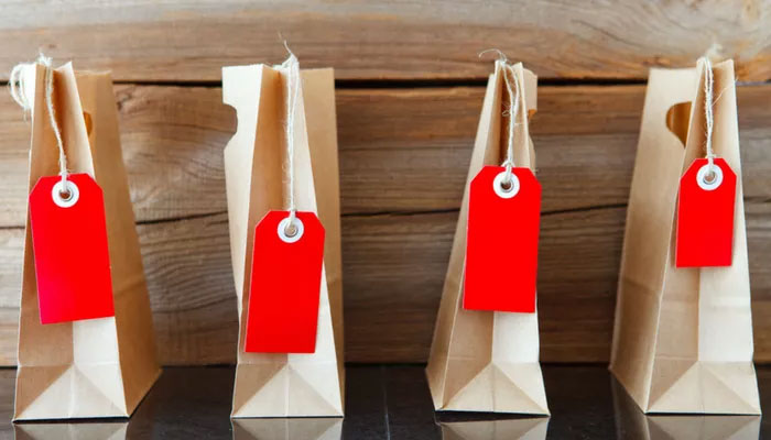 Preisforschungsmethoden sind unterschiedlich. Vier Papiertüten mit roten Preismarkierungen stehen vor einer Holzwand.