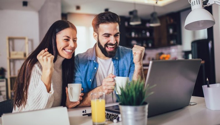 Ein Paar sitzt mit einer Tasse Kaffee in der Hand vor einem Laptop und freut sich über gelungenes Change Management.
