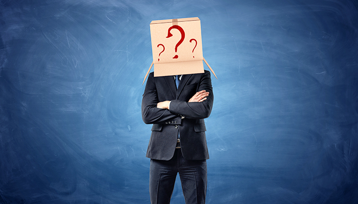 Ein Mann steht bei einer Exit Befragung mit verschränkten Armen und hat einen Karton mit roten Fragezeichen auf dem Kopf.