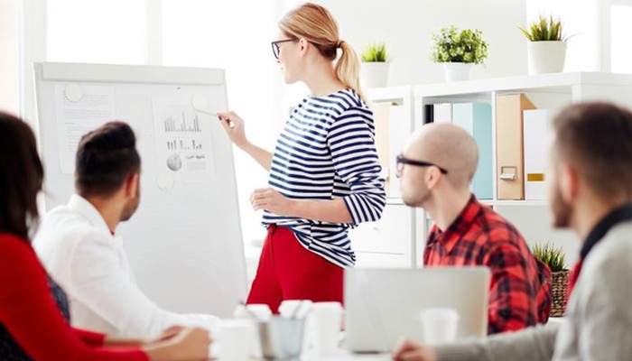 Eine Frau stellt ihrem Team die Ergebnisse der Führungskräfteentwicklung auf einem Whiteboard vor.