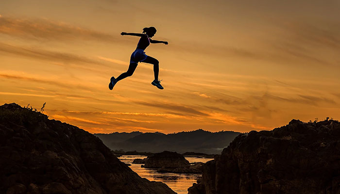 Eine sportliche Frau springt bei Sonnenuntergang über einen Fluss und symbolisiert damit wie man eine Gefährdungsbeurteilung durchführen kann.