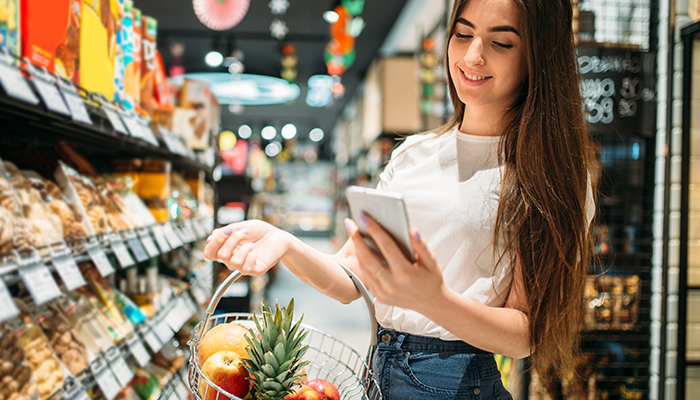 Eine junge Frau nimmt im Supermarkt an einer Konsumentenbefragung am Smartphone teil.