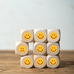Mehrere Würfel sind übereinander gestapelt und haben Sticker mit teils lachenden und teils weinenden Smileys aufgeklebt. Diese symbolisieren die Kundenbefragung.
