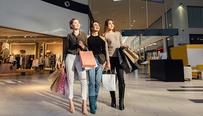 Drei Frauen mit Einkaufstaschen laufen durch ein Einkaufszentrum und zeigen wie erfolgreiche Kundenbindung zu Einkäufen führt.