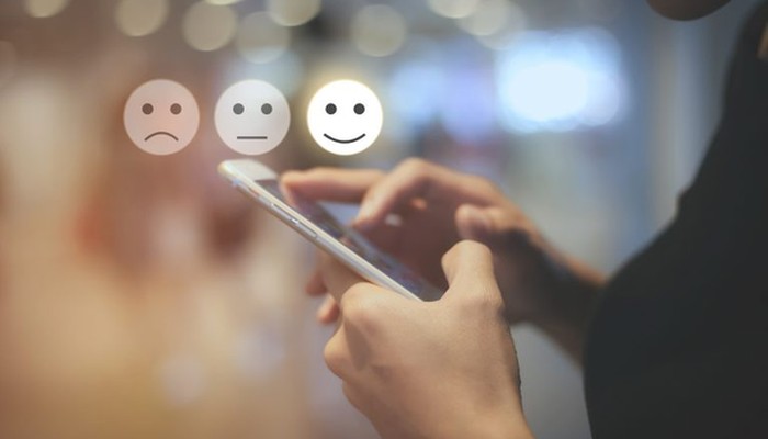 Eine Person tippt auf ihrem Smartphone auf einen zufriedenen Smiley und symbolisiert dadurch eine hohe Kundenbindung.