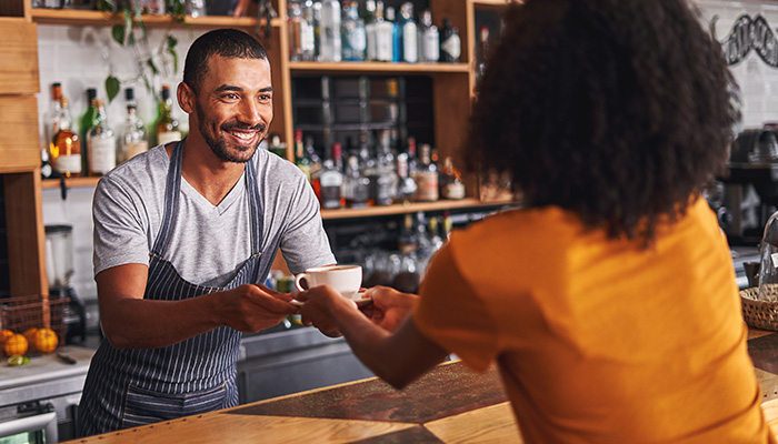 Kellner überreicht Frau lächelnd einen Kaffee: Vor einer Kundensegmentierung müssen zuerst Daten über die Interessen und Bedürfnisse gesammelt werden.