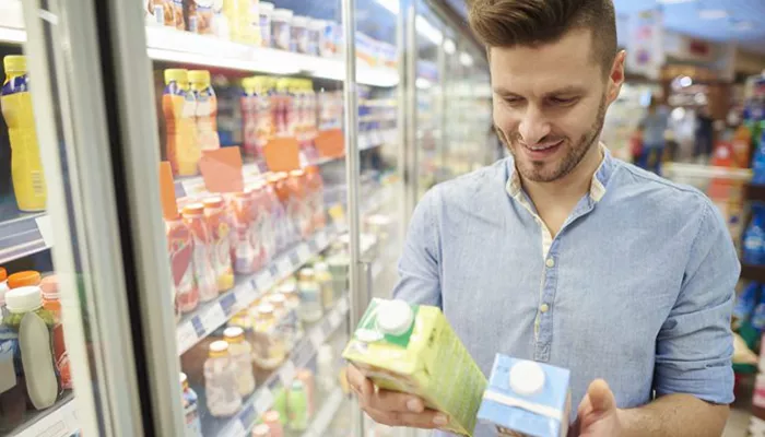 Ein Mann entscheidet sich vor einem Kühlregal zwischen zwei Milchprodukten, ein Verhalten welches im Rahmen der Forschung zur Markenbekanntheit beobachtet wird.