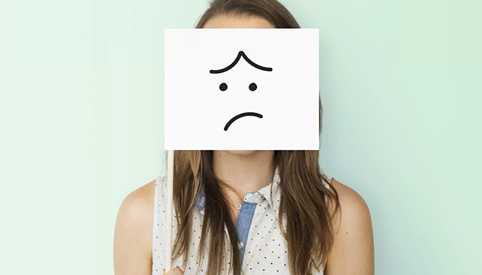 Eine Frau hält ein Schild mit einem traurigen Smiley vor ihr Gesicht. Dies symbolisiert, dass negative Ergebnisse berücksichtigt werden müssen, um die Mitarbeiterbindung zu fördern.