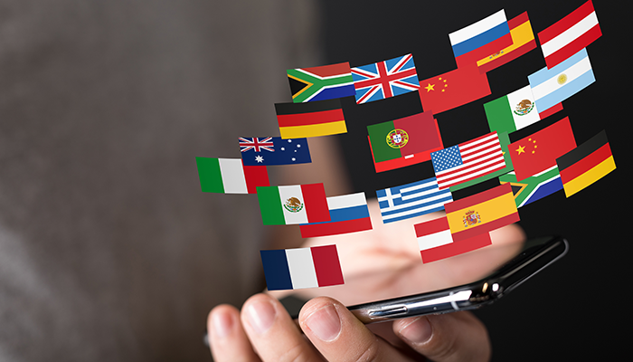 Über einem Smartphone schweben Flaggen unterschiedlicher Länder, die für eine internationale Mitarbeiterbefragung ausgewählt wurden.