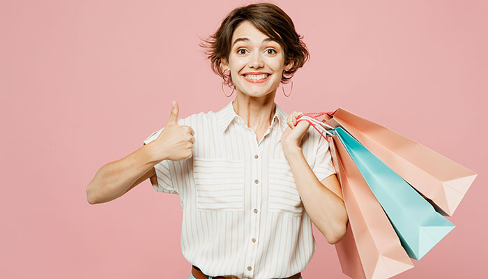 Dank dem Verbraucherpanel können Unternehmen zufriedene Konsumenten befragen. Eine Frau strahlt, hebt ihren Daumen und hat Einkaufstaschen in der Hand.