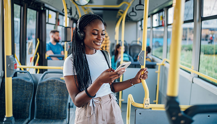 Eine Frau steht in einem Bus und schaut auf Ihr Smartphone und öffnet das Deutschland-Ticket