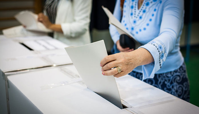 Teilnehmende stecken bei betriebliche Wahlen die Wahlunterlagen in Urnen.
