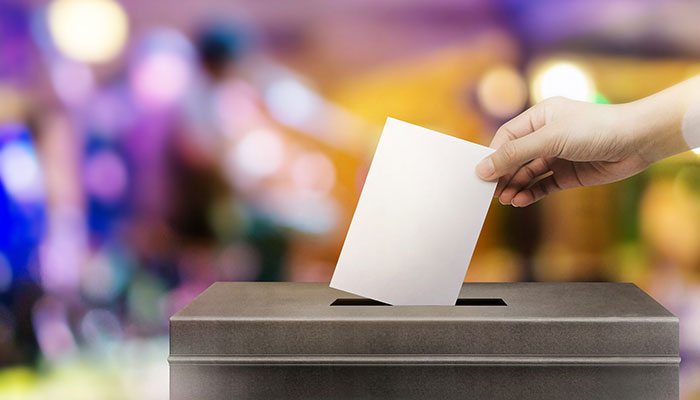 Betriebs-Wahlen sinnvoll durchführen. Ein Mann steckt einen Zettel in eine Wahlurne.
