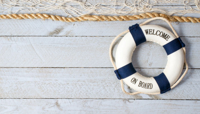 Ein blau-weißer Rettungsring mit dem Schriftzug Welcome on Board liegt auf einem Holzboden und symbolisiert das Onboarding im Unternehmen.
